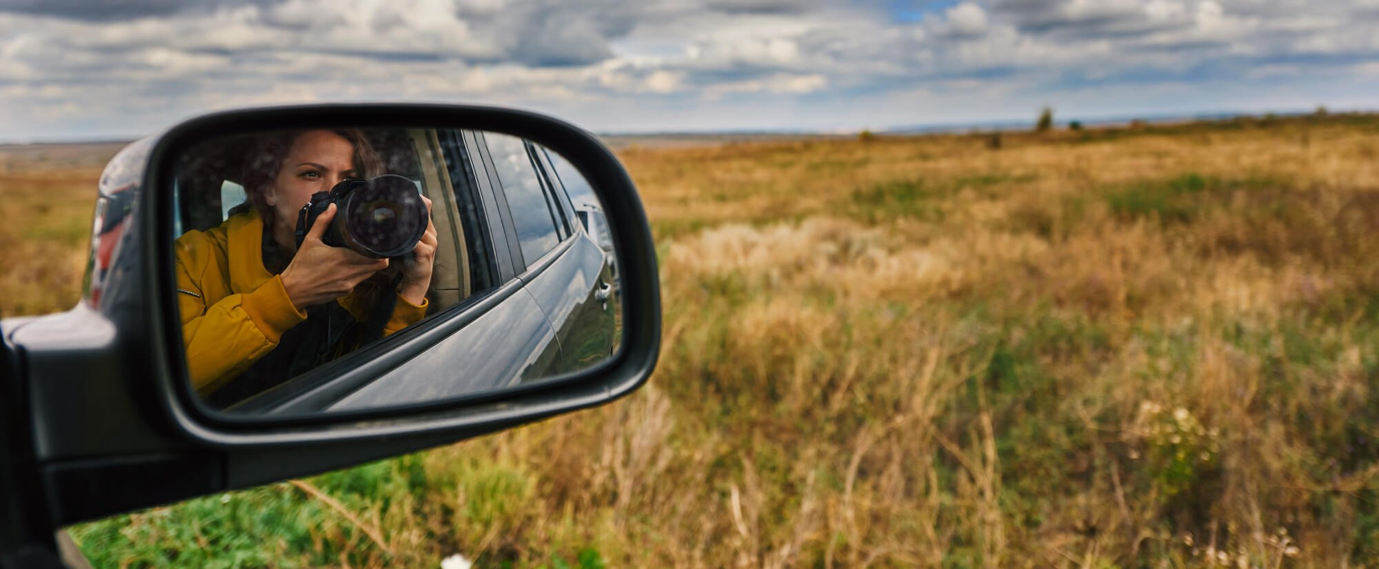 A photographer framed in a car mirror on the open road